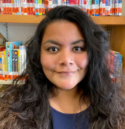 Headshot of Lorena Romero, a Latinx woman with long, brown, curly hair with a bookshelf behind her 