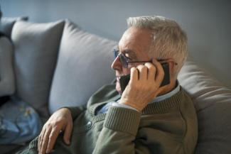 Image of person sitting on sofa holding phone by left ear